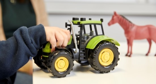A child holding a toy tractor and horse)